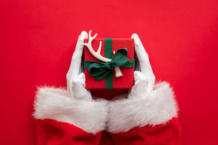 Santa Claus holding a wrapped gift box present against a red backgroundの写真素材