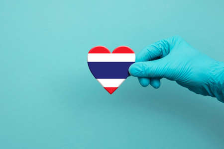 Medical workers hand wearing surgical glove holding Thailand flag heartの写真素材