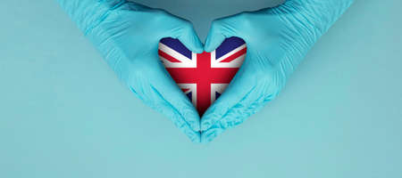 Doctors hands wearing blue surgical gloves making hear shape symbol with United Kingdom flagの写真素材
