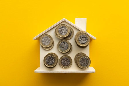 Cost of living background. United Kingdom pound coins on a wooden houseの写真素材