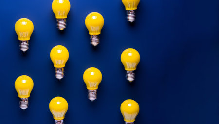 Overhead flat lay view of a collection of glowing yellow light bulbs on a blue backgroundの素材