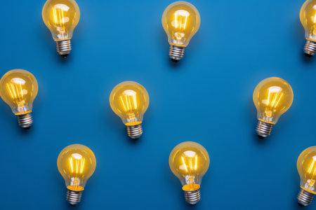Overhead flat lay view of a collection of glowing yellow light bulbs on a blue backgroundの素材