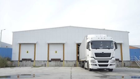 Semi-trailer truck standing at warehouse ramps for load or unload goods at dock logistics park. Truck in parking near warehouse.の写真素材