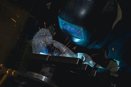 Close-up blacksmith welder in protective mask works with metal steel and iron using a welding...