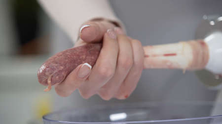 Woman cooks sausages in traditional way using sausage filler of electric mincer machine. Production of meat delicacies at home. Preparation of raw beef sausages with electric grinder.の写真素材