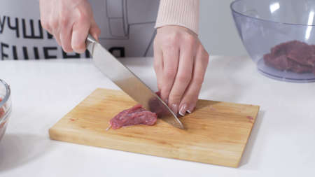 Woman cutting raw meat on small pieces with kitchen knife cutting board. Female cutting red beef filet on wooden board, holding knife in hand. Housewife is cooking at home interior. Concept: foodの写真素材