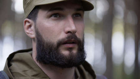 Portrait of handsome young man hunter or tourist. Man in camouflage clothes hunts outdoor in forest hunting alone. Close up of man hiker standing in forest. Hunter hunts down preyの写真素材
