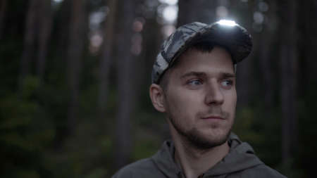 Portrait of handsome young man hunter or tourist. Man puts on his head cap with diode flashlight on...