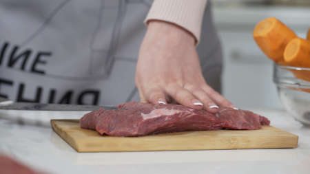 Woman cutting raw meat on small pieces with kitchen knife cutting board. Female cutting red beef...