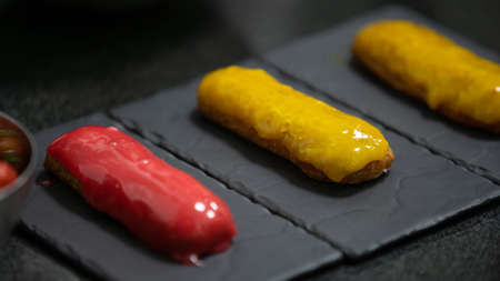 Yellow and pink glaze eclair on stone plates. Modern desserts and cakes. Cupcakes with cream...