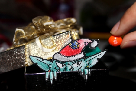 Green Evil elf with christmas hat popping out of christmas box while looking at candyの写真素材