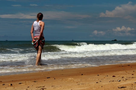 Rear view of female walking along the shore enjoying small current wavesのeditorial素材