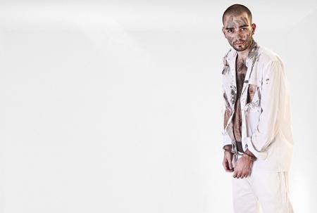 offender in handcuffs. hi dressed in a torn white shirt dirty. a man is in a light roomの写真素材