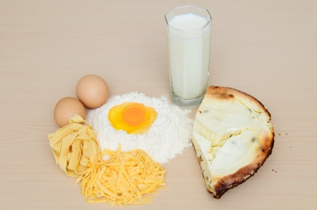 Egg yolk on flour and pasta, cheese, a glass of milk, cheesecake on wooden background の写真素材