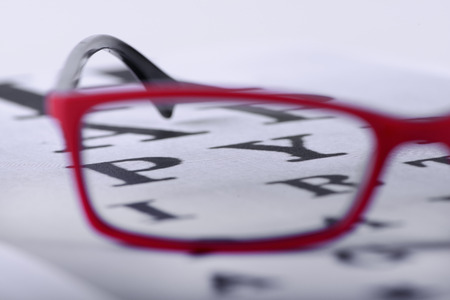 Reading red eyeglasses and eye chart close-up on a light background