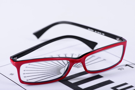 Reading red eyeglasses and eye chart close-up on a light background