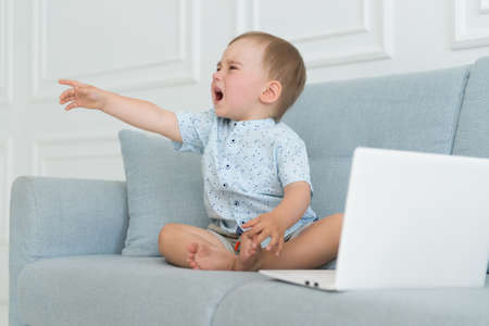 sad baby crying near laptop - tantrum child on a sofa