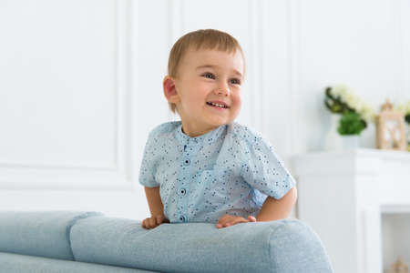 portrait of a little smiling boy child playing on the sofa in the living roomの写真素材