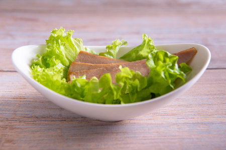 tuna slices with fresh green lettuce in white plate on wooden background closeupの写真素材