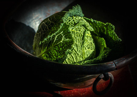 savoy cabbage in a vintage bowl on which fall the rays of sun light on a dark backgroundの写真素材
