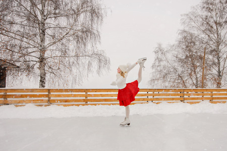 Child young girl ice skating at the ice rink outdoor. The girl in the red skirtの写真素材