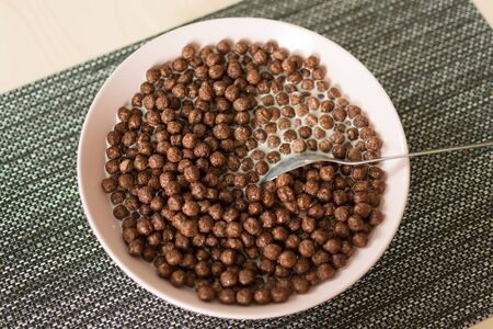 Chocolate cereal balls with milk in a bowl on napkin on wooden table. Dry breakfast cereal balls. Healthy breakfast concept.の写真素材