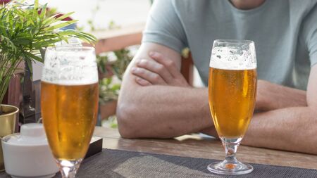 Two glasses of beer on table against part view man. Man drink beer in cafe.の写真素材