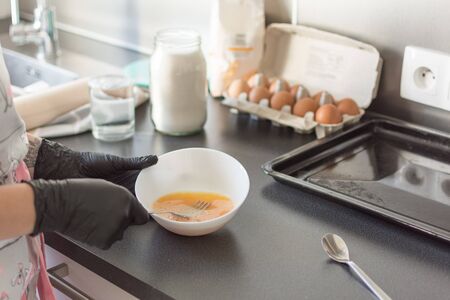 Woman hands beating eggs in a bowl with fork. Process of beating eggs. Food ingredients for baking: flour, eggs, milk, sugar.の写真素材