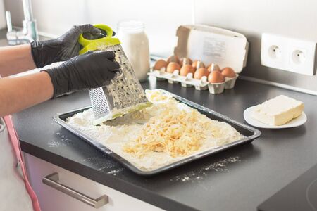 Woman hand grating butter for baking pie. Process of baking. Food ingredients for baking: flour, eggs, milk, sugar, butter.の写真素材