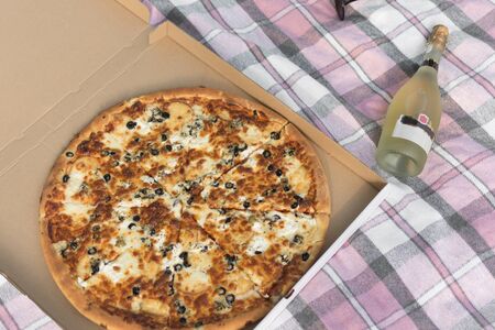 Pizza in a cardboard box top view and a bottle of champagne. Pizza delivery. Picnic concept.の写真素材
