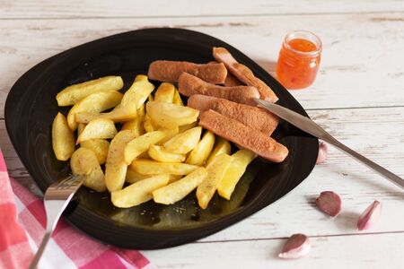 French fried potatoes on black plate with sauce on wooden table. Tasty french fries. Baked potatoes by slices.の写真素材