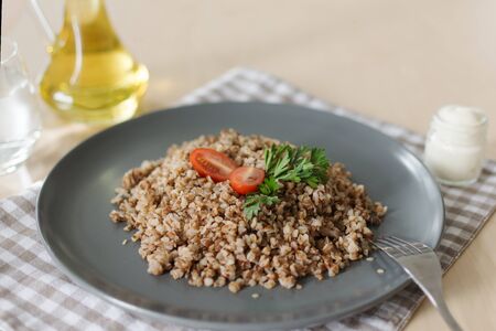 A plate with buckwheat porridge with tomato and parsley. Olive oil and sour cream for dressing.の写真素材