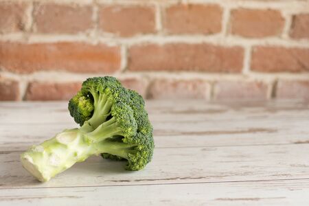 Bunch of fresh green broccoli on wooden background against brick wall closeup. Healthy eating concept.の写真素材
