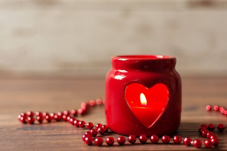 Heart-shaped red candlestick with candle decoraded with bead chain on wooden background. Valentines day concept. Copy space.の写真素材