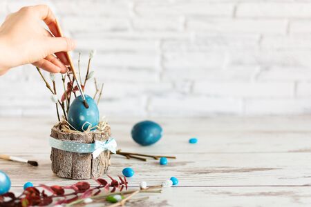 Woman hand paint Easter egg with paintbrush in modern marble classic blue color on wooden table....