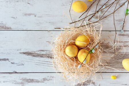 Yellow colored Easter eggs on wooden table in a nest. Happy Easter time. Creative Easter decoration top view. Copy space.の写真素材