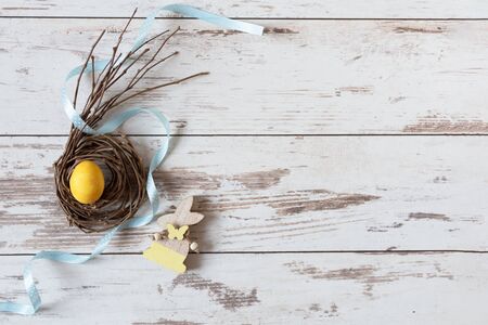 Yellow Easter egg in a creative nest with ribbon on wooden table top view. Happy Easter time....
