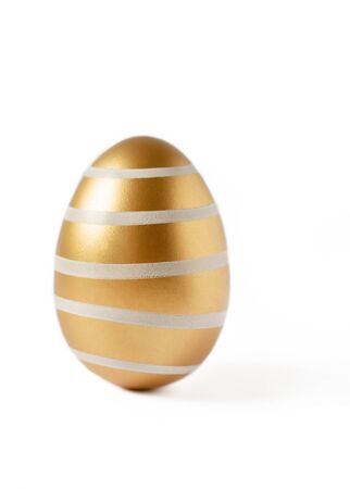 Golden colored easter egg isolated on white background. Modern easter egg painted in a fashion golden color. Happy Easter time.の写真素材