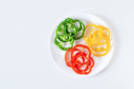 Set of colorful sliced bell pepper on plate on white background top view. Slices of red, yellow and...