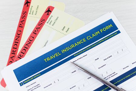 Travel insurance claim form with a boarding pass and passport on white wooden table. Travel policy...
