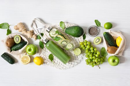 Various green fruits and vegetables with bottles of smoothie and infused water on white wooden table top view. Eco friendly shopping concept. Detox diet.の写真素材