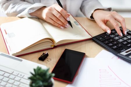 Woman hands counting with calculator and making notes to notebook. Finances, economy concept. Office workplace in white colors.の写真素材