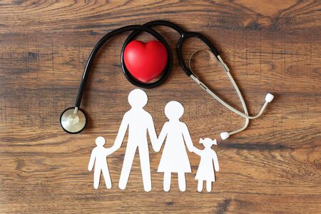 White paper cut of family, stethoscope and heart on wooden background top view. Health medical insurance concept.の写真素材