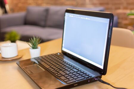 Laptop computer with blank screen and a cup of coffee on table at home interior in the evening. Working during night, freelance concept.の写真素材