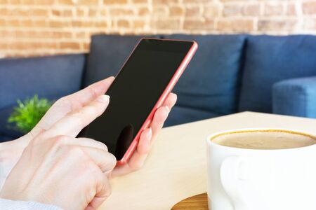 Woman hand using smartphone against home interior. Freelance or blogging concept. Coffee break.の写真素材