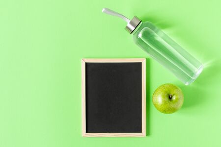 Bottle of water with green apple and chalkboard for text on green background top view. Healthy lifestyle concept. Diet planning. Copy space.の写真素材