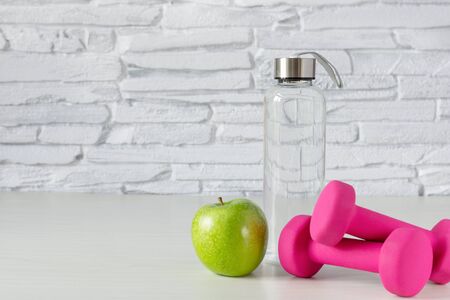 Pink dumbbells, bottle of water and green apple on white wooden table. Healthy lifestyle concept. Sports. Copy space.の写真素材