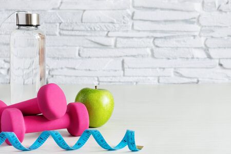Pink dumbbells, bottle of water and green apple on white wooden table. Healthy lifestyle concept. Sports. Copy space.の写真素材