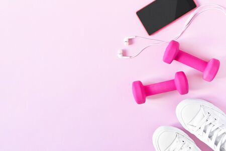 Fitness equipment top view with copy space. Fitness concept. Dumbbells, smartphone and sneakers on pink background. Fitness background, healthy lifestyle.の写真素材