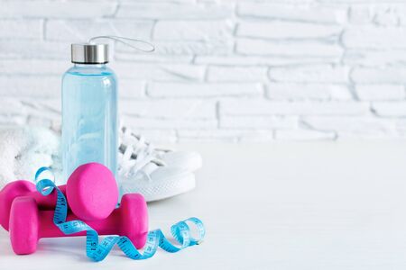Pink dumbbells, bottle of isotonic drink, sneakers and measurenment tape on white wooden table. Healthy lifestyle concept. Sports. Copy space.の写真素材